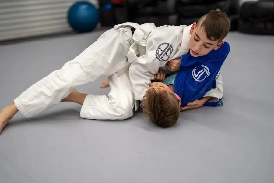 Two boys practicing Brazilian Jiu Jitsu side control technique during kids class