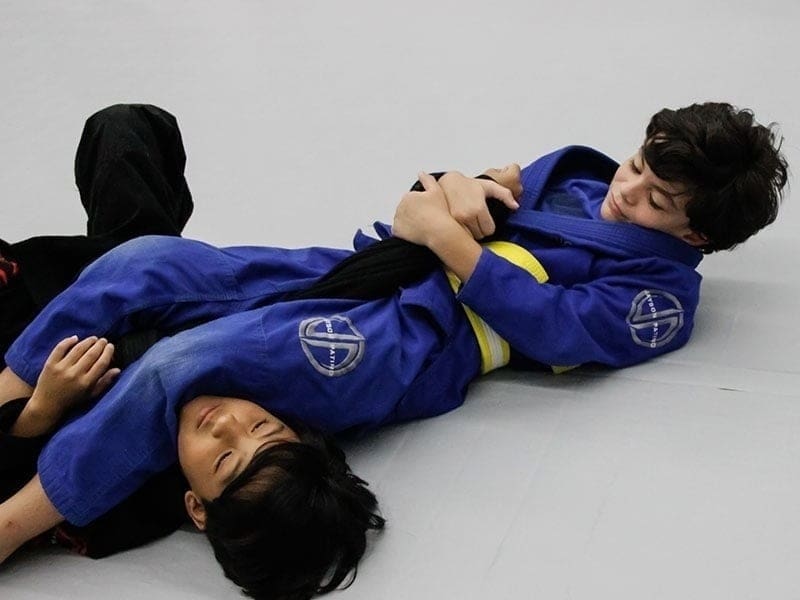 Two young students drilling armbar technique in youth BJJ class