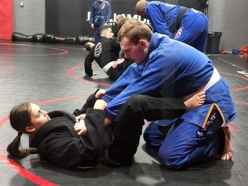 An adult instructor and student demonstrating a guard pass technique in a brazilian jiu jitsu class at a martial arts academy.