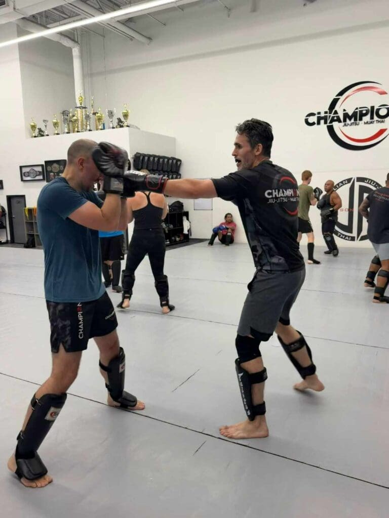 A male martial arts practitioner throwing a jab at a sparring partner holding a high guard during a gym striking drill, applying Adults Brazilian Jiu Jitsu position strategy.