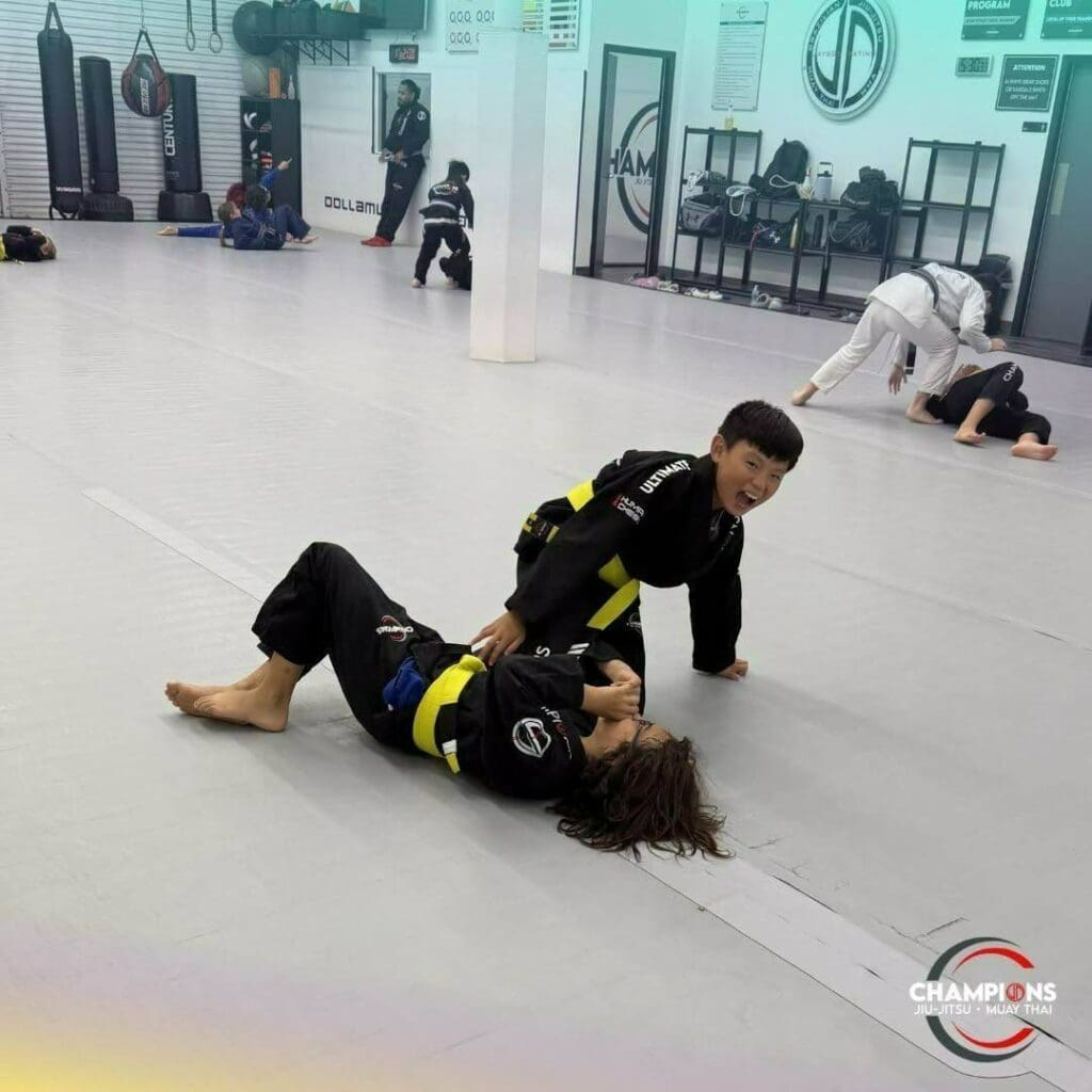 Young Brazilian Jiu-Jitsu students practicing a ground grappling position during class while developing martial arts training fundamentals.