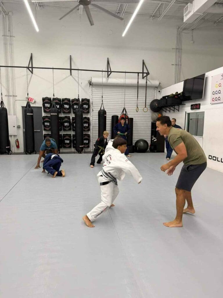 Young Brazilian Jiu-Jitsu student practicing a playful control position with an instructor during class while learning martial arts training fundamentals.